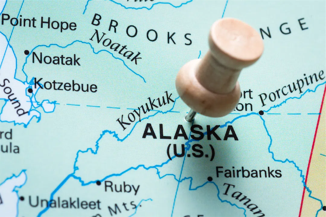 A push pin marks Alaska on a world map, highlighting it as a real estate destination.